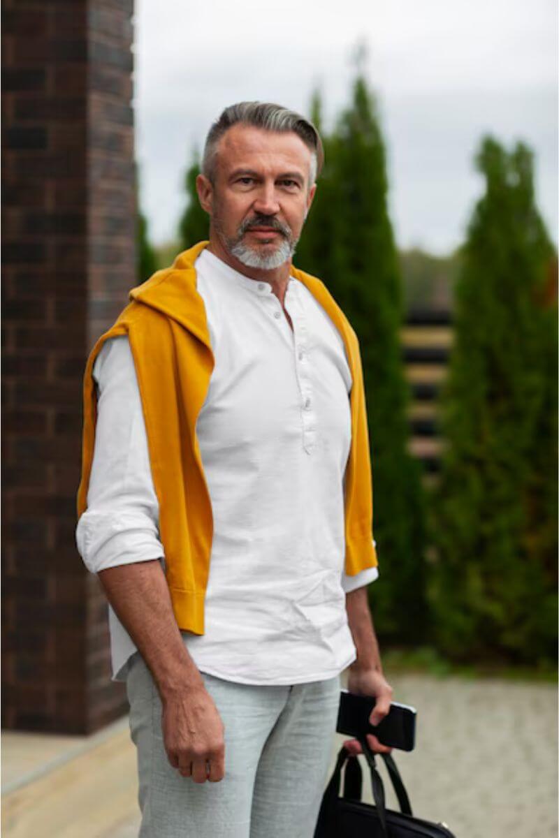 Middelbare man in witte blouse met gele trui in de tuin, casual en betrouwbaar